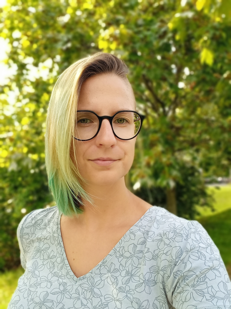 This picture shows the game scholar Dr. Agata Waszkiewicz in front of a lush green background of trees and hedges,