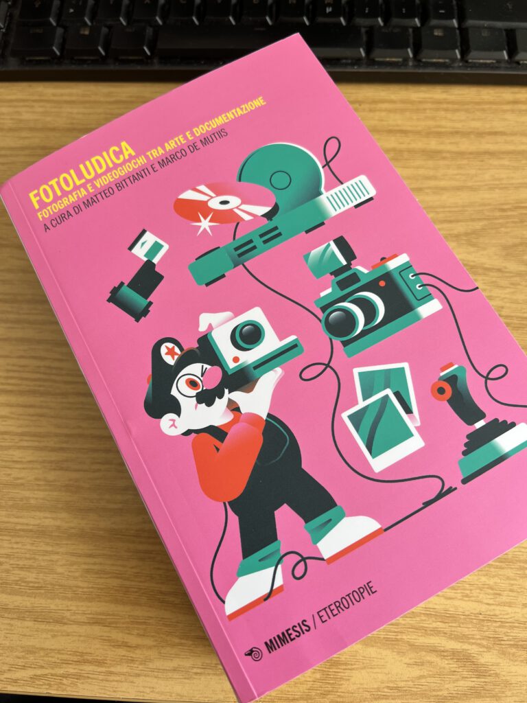 A pink book titled "FOTOLUDICA" with a subtitle in Italian. The cover illustration features a cartoon character holding various photography equipment, including cameras and film rolls. The book is placed on a wooden surface next to a black keyboard.